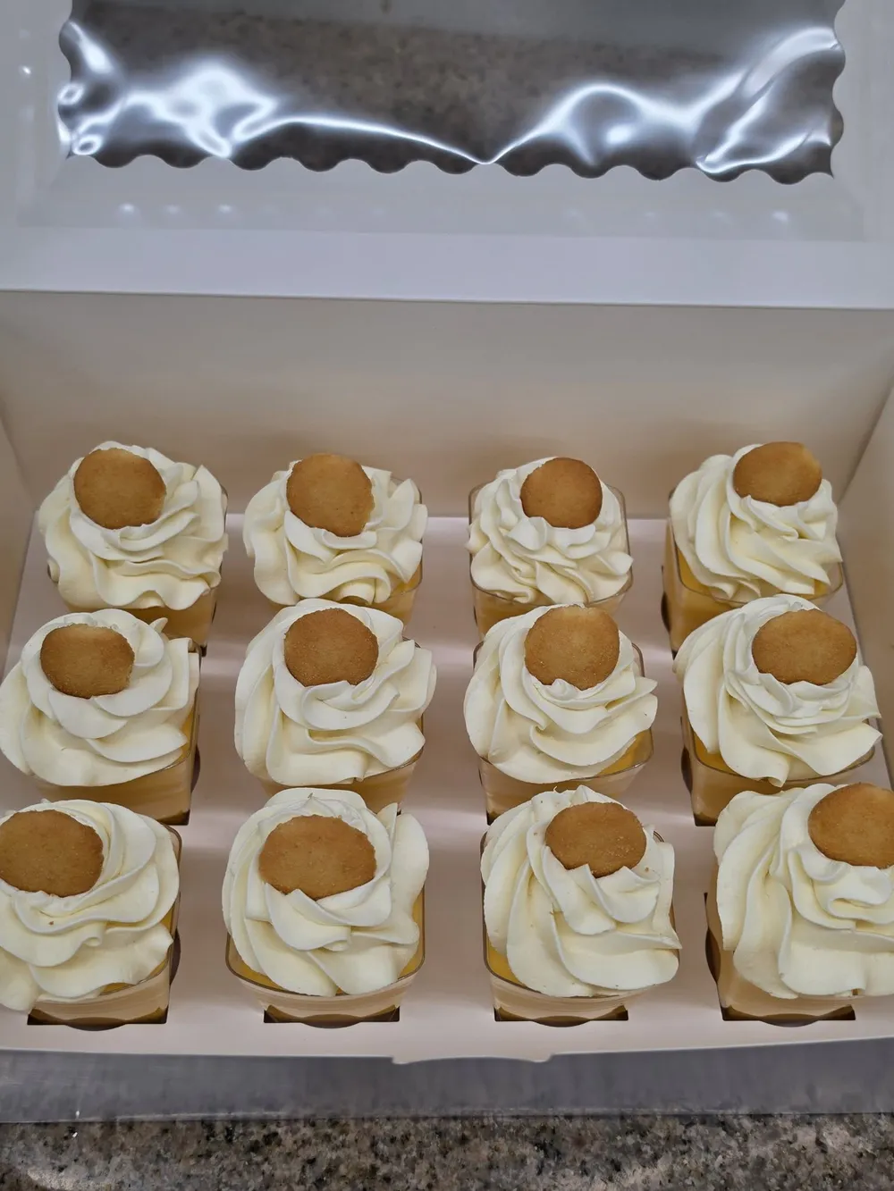 A box of banana pudding cups topped with whipped cream and a vanilla wafer